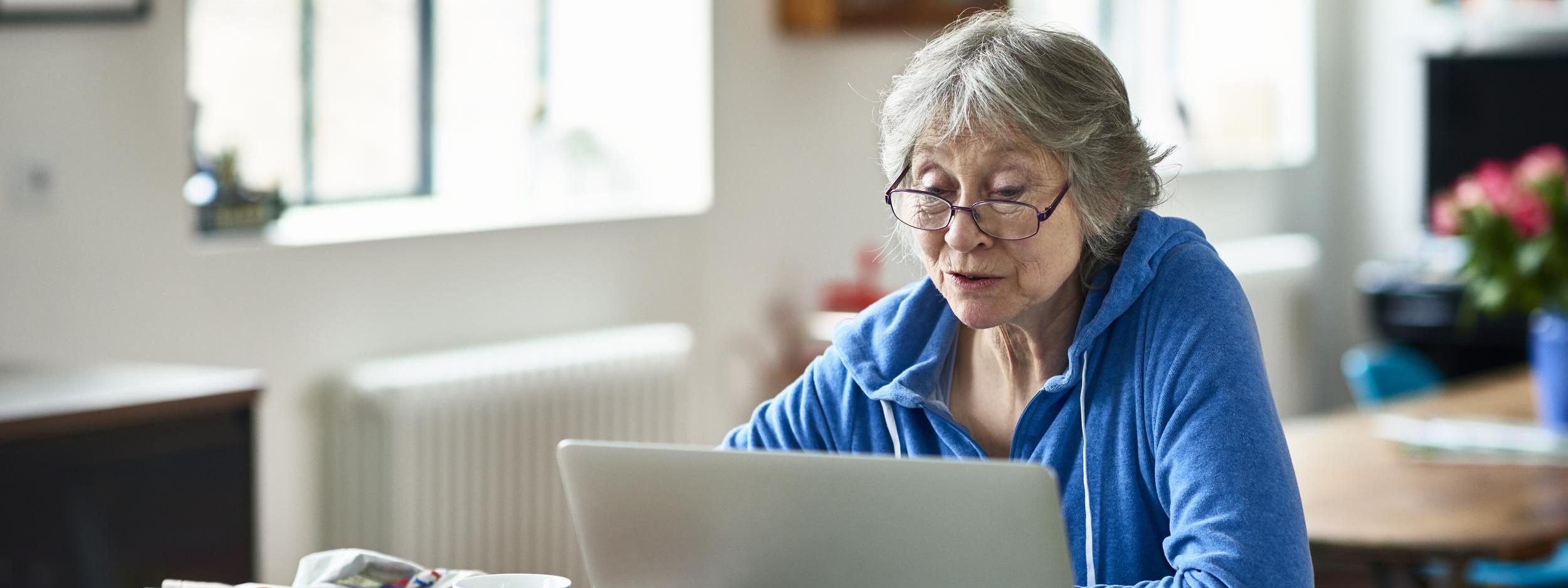 Senior woman wearing glasses using laptop at home